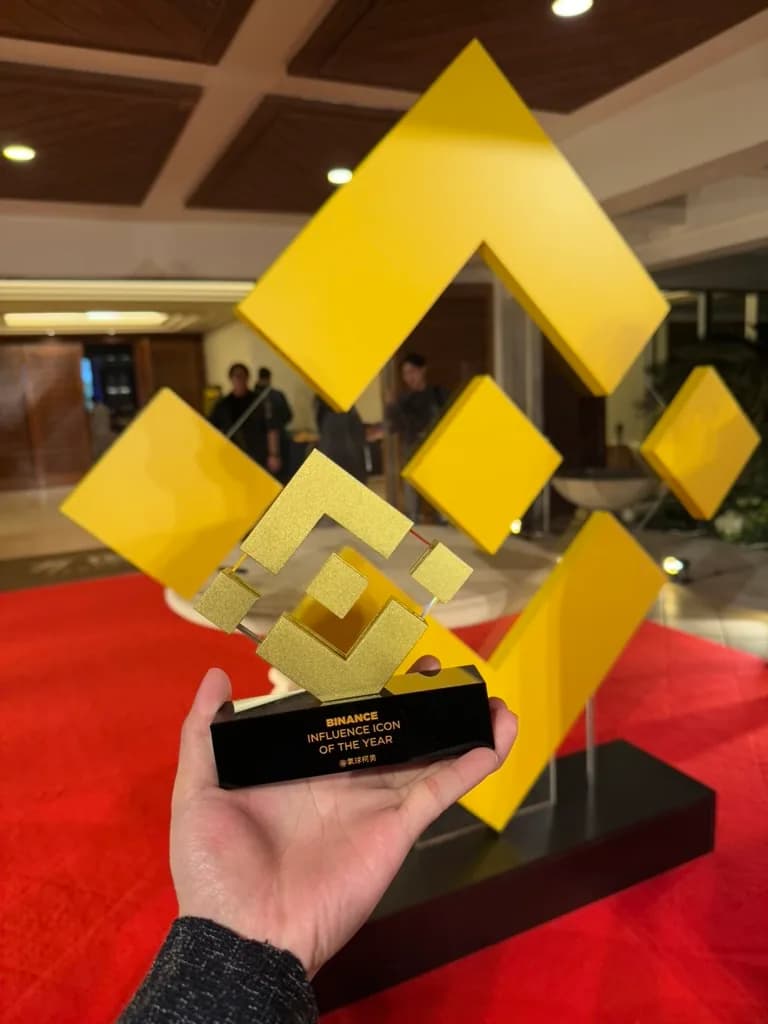 幣安 Influence Icon of the Year 獎座特寫，底座刻有「@氣球柯男」，背景為大型幣安標誌裝置