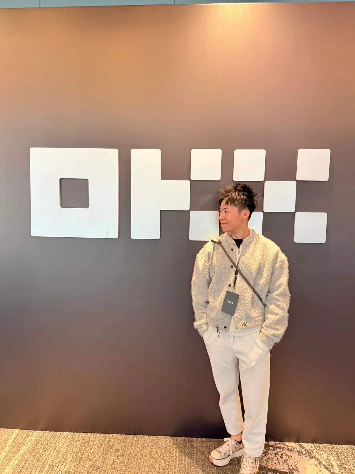 氣球柯男在 OKX 品牌牆前留影，掛 OKX 識別證