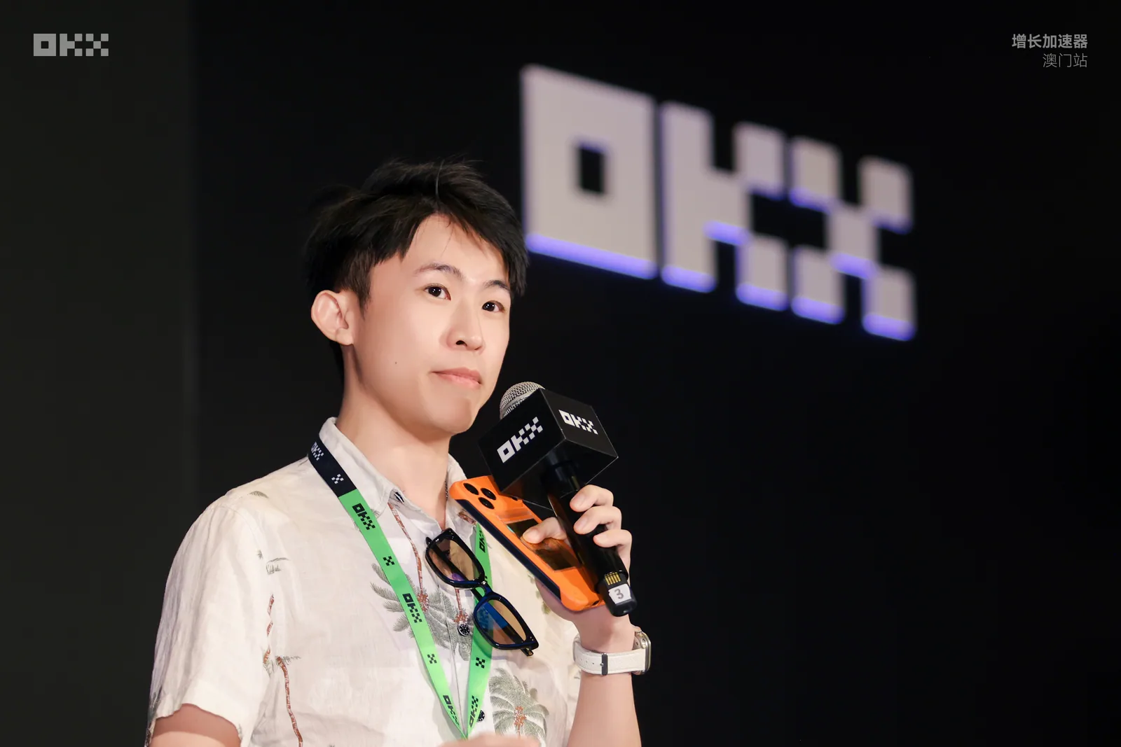 氣球柯男在 OKX 增長加速器澳門站舞台上手持 OKX 麥克風演講