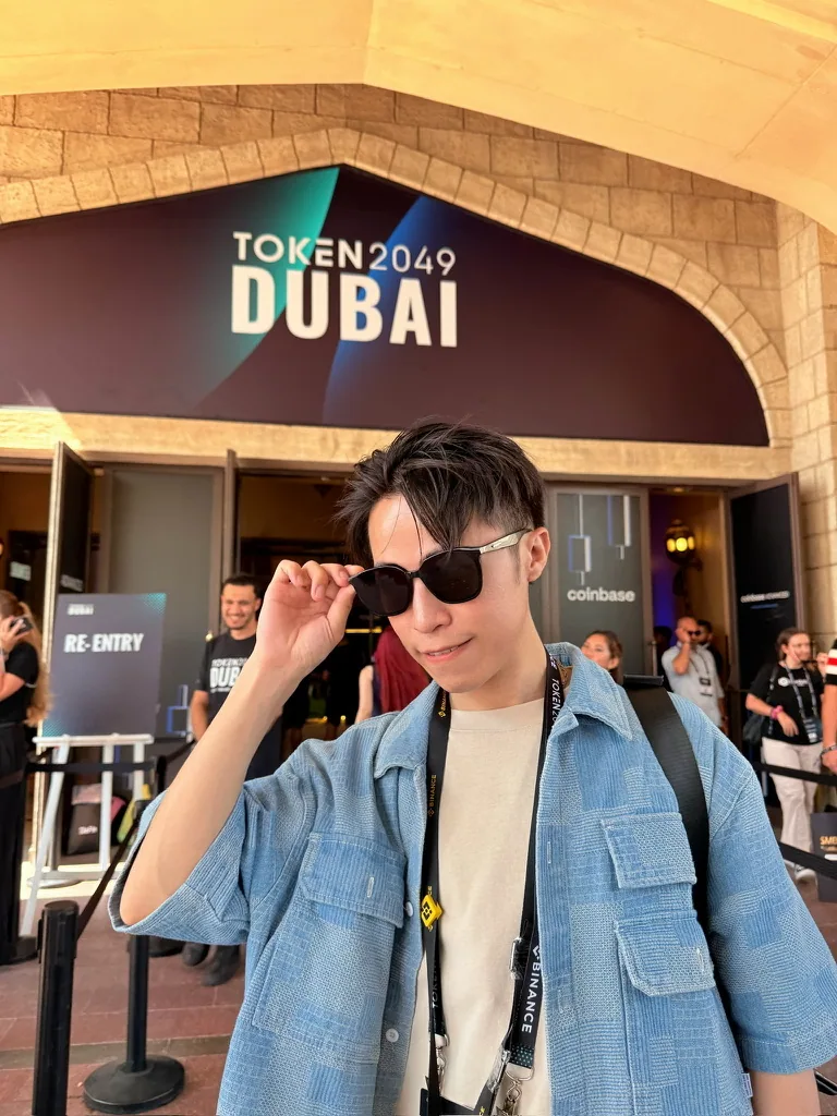 氣球柯男在 TOKEN2049 Dubai 會場入口前,戴墨鏡、掛活動識別證